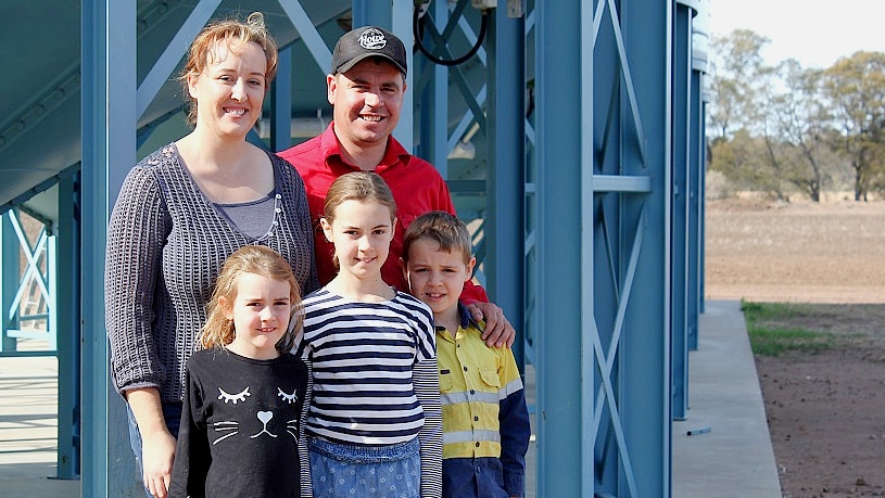 Brad Jackson, his wife and three children stand underneath their blue silos.