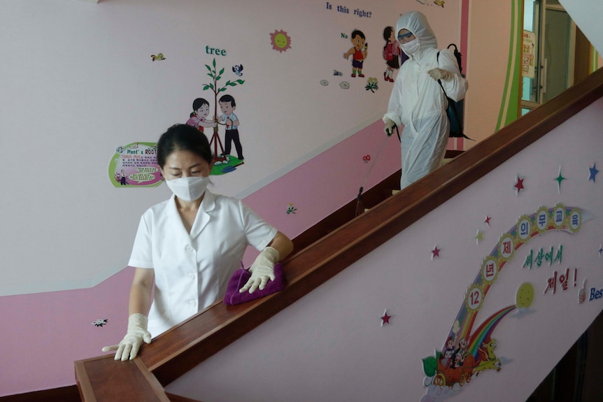 A woman in a face mask runs a sponge over a hand rail on a staircase 