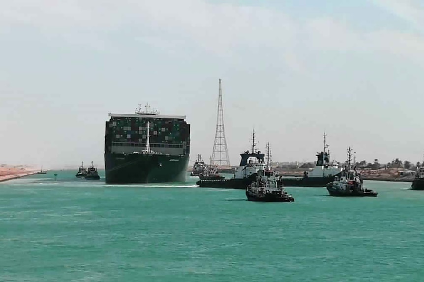 The Ever Given cargo ship navigates through the Suez Canal, flanked by tugboats