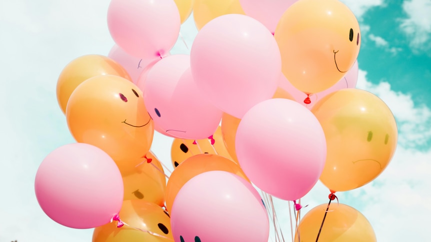 A bunch of pink and yellow balloons with smiley and frown-y faces. 