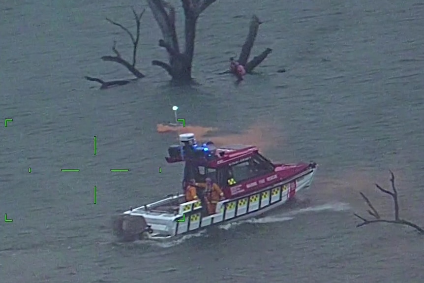 A police boat and people holding onto a tree.
