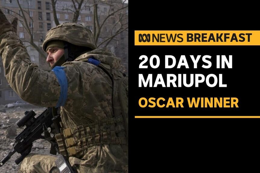 20 Days in Mariupol, Oscar Winner: A man in combat fatigues holds is arm up. He is holding a rifle in his other arm.