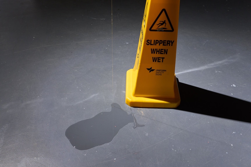 A string of drool pools on the floor next to a warning sign that says 'SLIPPERY WHEN WET'.