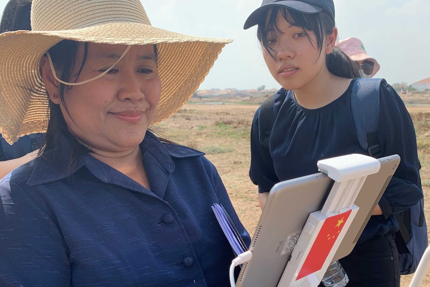 A woman holds a device connected to an iPad as another woman looks over her shoulder