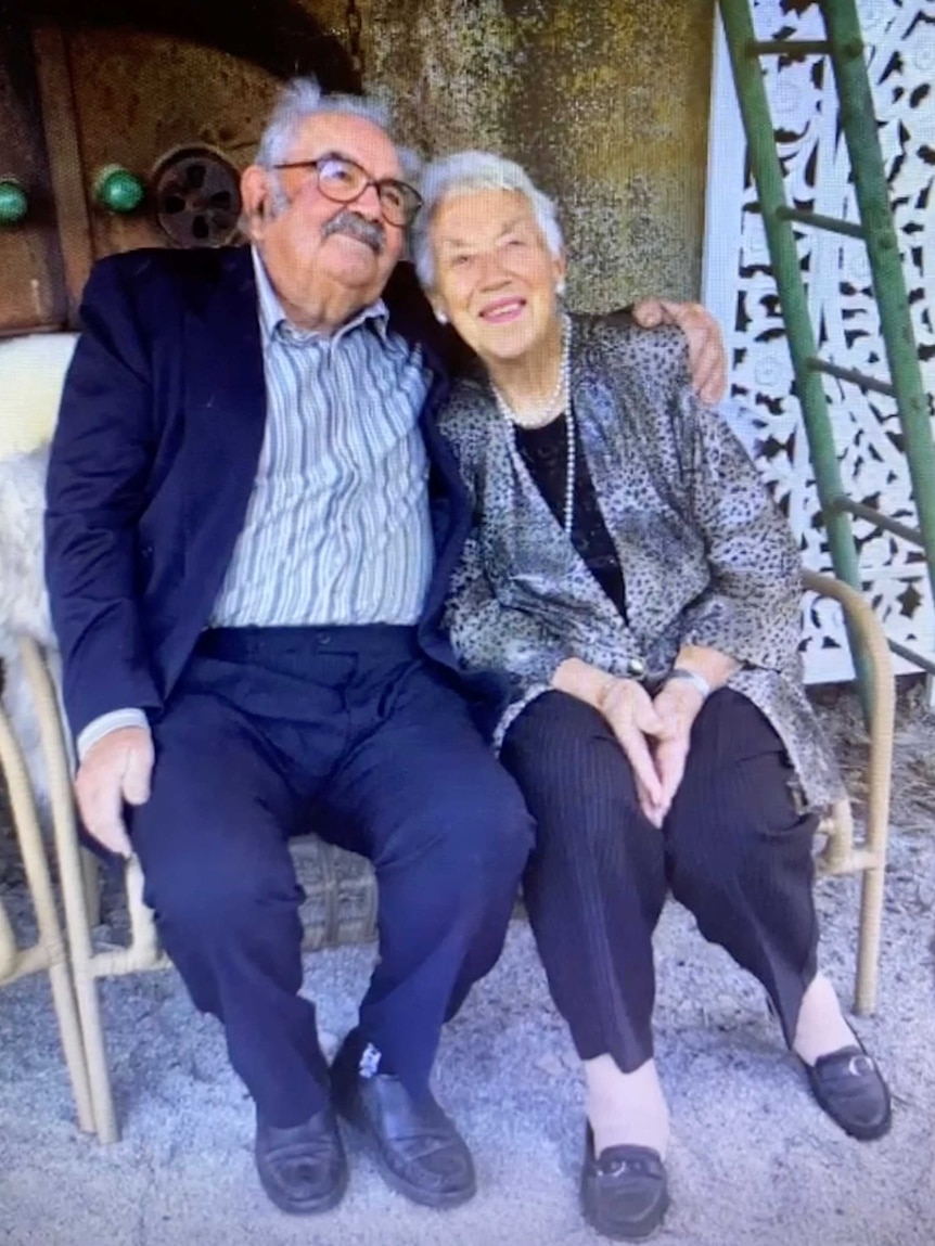 old man with glasses in suit puts arm around old woman wearing leopard print jacket and pearls