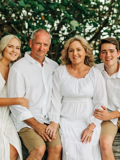 A family portrait under trees of a couple and their young adult children. All smiling and dressed in white.