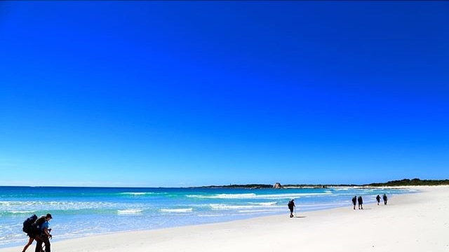 Bush walkers carrying backpacks walk along Bay of Fires Beach on Tasmania's east coast.