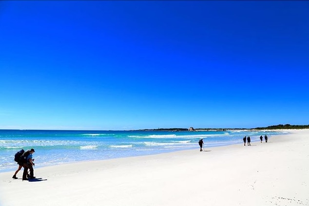 Bush walkers carrying backpacks walk along Bay of Fires Beach on Tasmania's east coast.