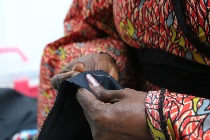 A close-up shot of a woman's hands as she sews with a needle.