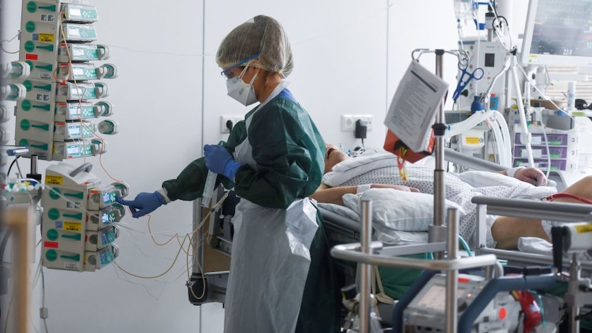 A female health worker in full PPE cares for a COVID-19 patient.