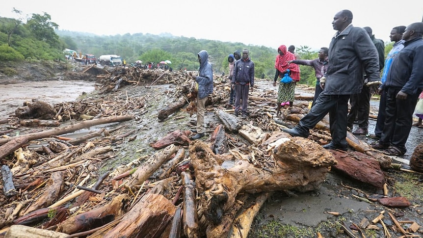 Passengers from stranded vehicles stand next to the debris from floodwaters, on the road from Kapenguria,