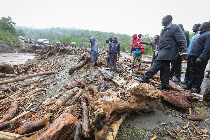 Passengers from stranded vehicles stand next to the debris from floodwaters, on the road from Kapenguria,