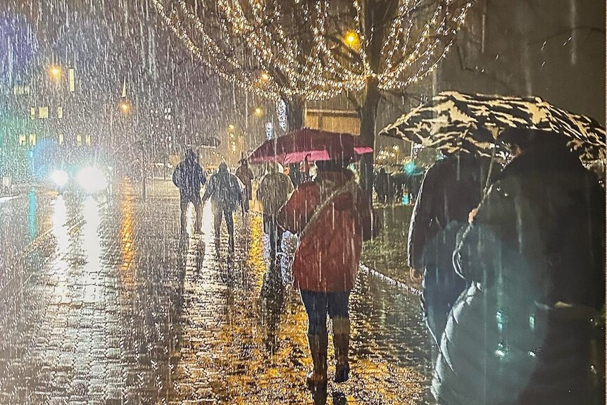 people holding umbrellas walk through rain in the night