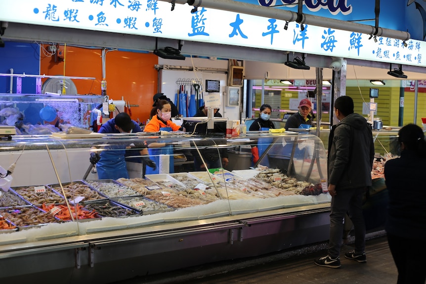 Masked fishmongers serve customers, underneath a banner of Chinese characters.