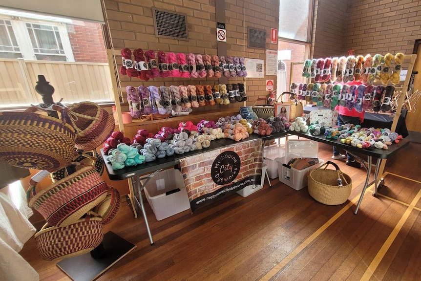 An indoors market stall displaying a variety of coloured wool skeins and woven baskets.