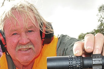 Paul Cors with his hand on the scope of a gun wearing protective ear muffs.