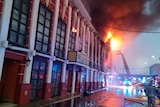 Firefighters use an extended ladder to reach up to an historic-looking building on fire.