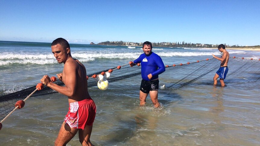 Commercial fisherman holding nets in water on Port Macquarie beach.