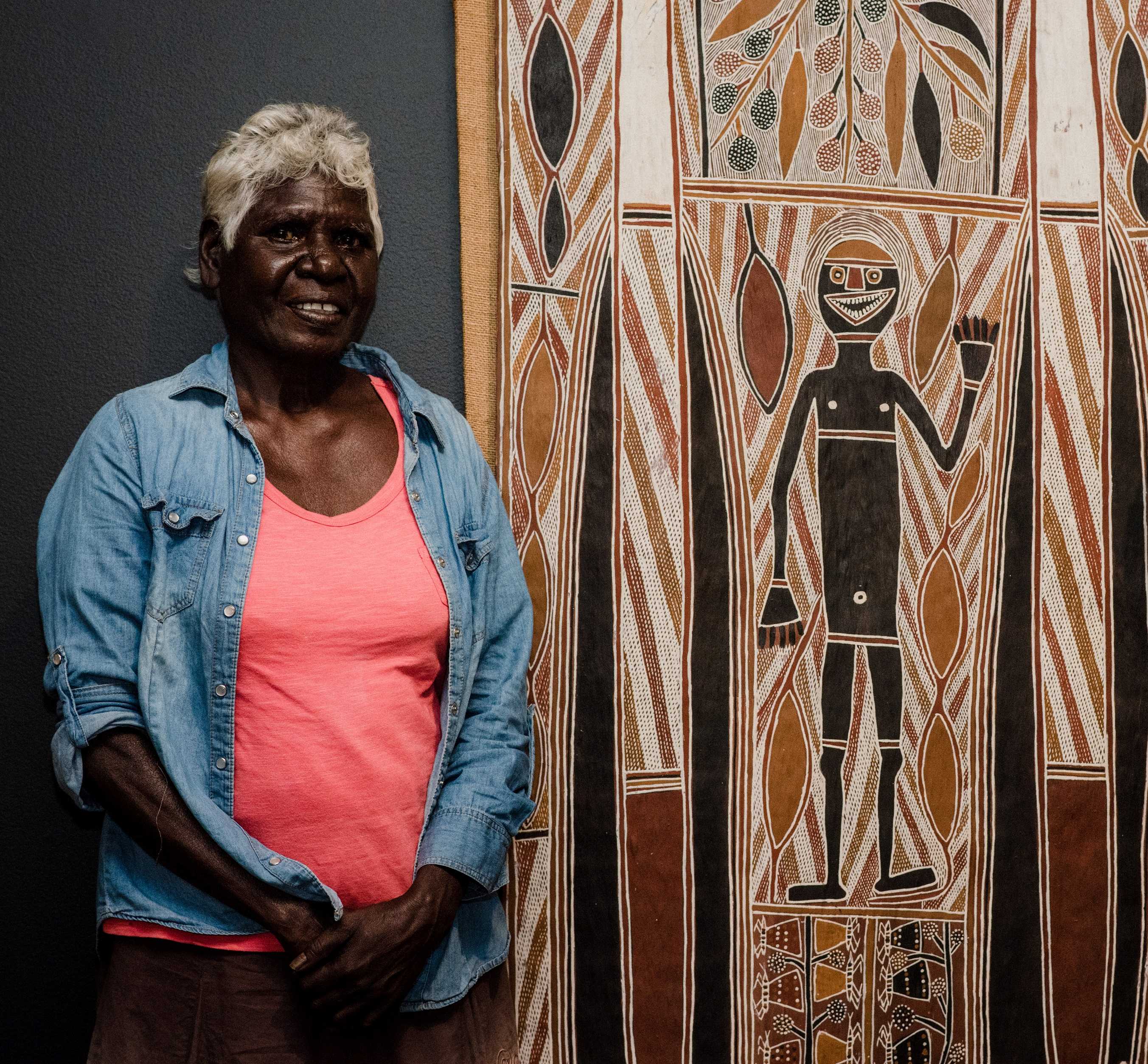 Lady standing next to a bark painting.
