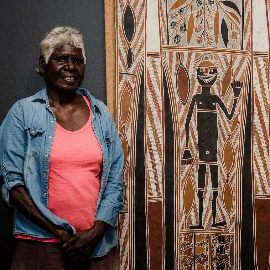 Lady standing next to a bark painting.