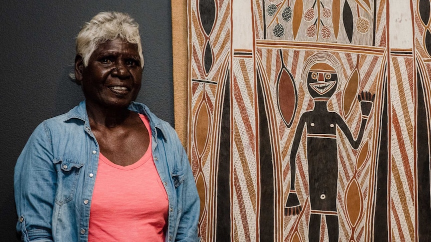 Lady standing next to a bark painting.