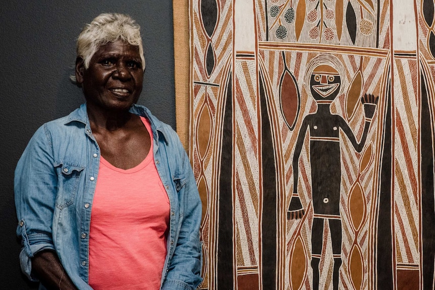 Lady standing next to a bark painting.