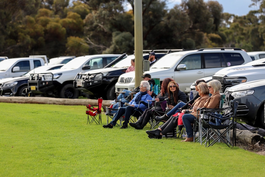 A row of woman in fold out chairs sitting on grassed oval