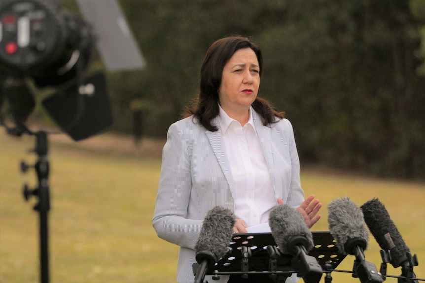 Annastacia Palaszczuk wearing a blazer speaks in from of media microphones