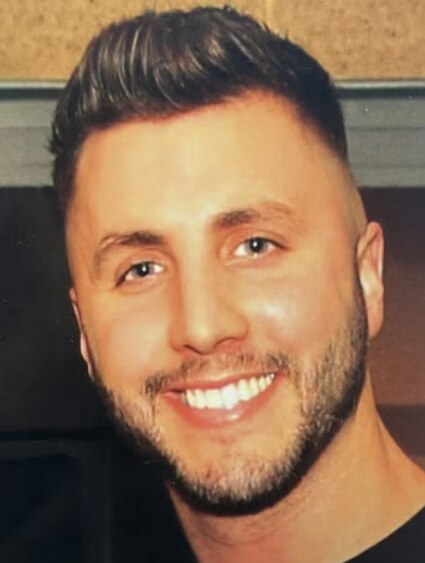 A man with short brown hair and a short beard smiling.