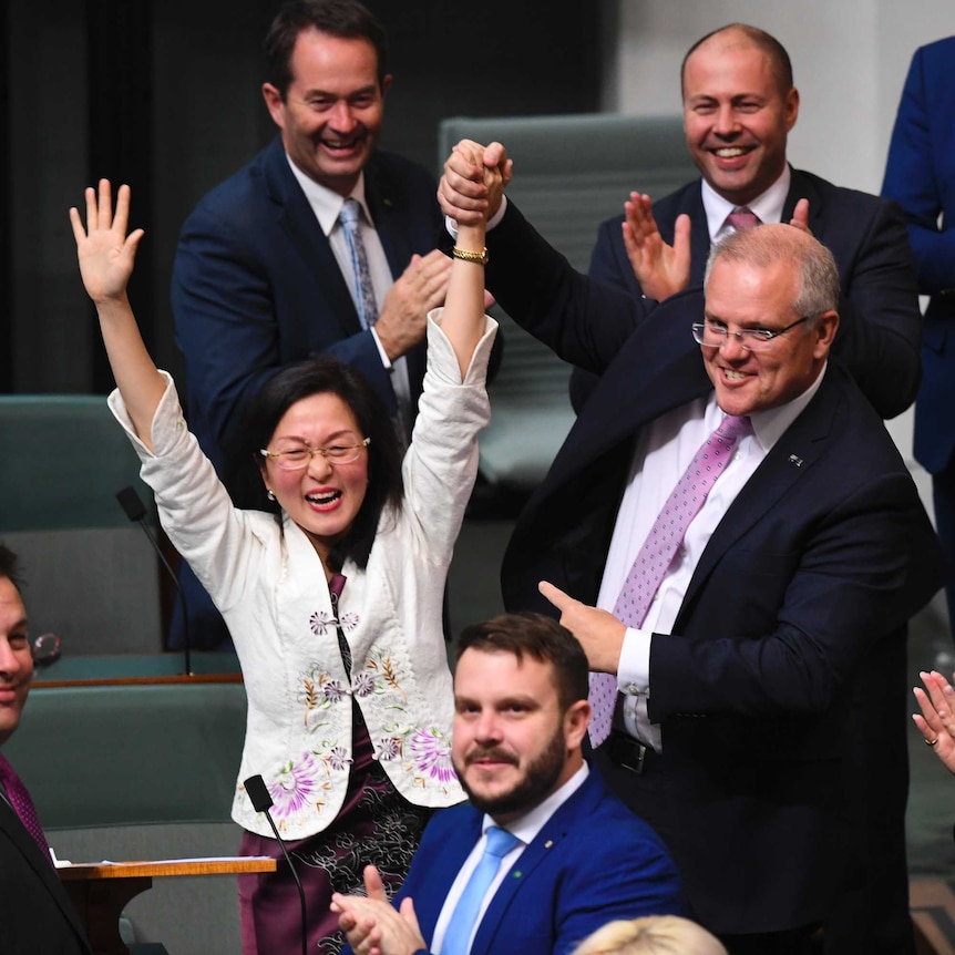Gladys Liu wearing white jacket smiles with hands raised above head, next to Scott Morrison, wearing suit in Parliament