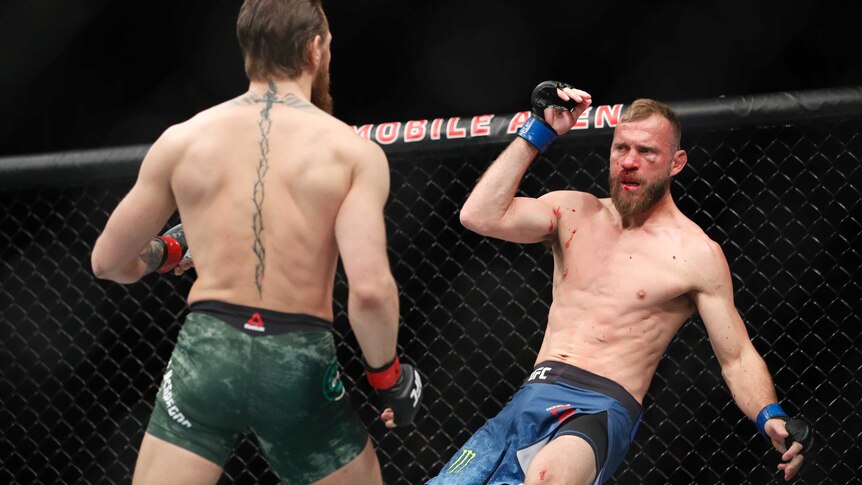 Donald 'Cowboy' Cerrone falls backwards as Conor McGregor watches on in the octagon