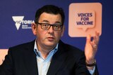 Daniel Andrews gestures with a hand as he speaks in front of a 'Voices for Vaccines' purple backdrop.