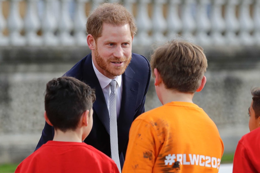 Prince Harry shakes the hand of schoolchildren who are wearing shirts emblazoned with "#RLWC2021".