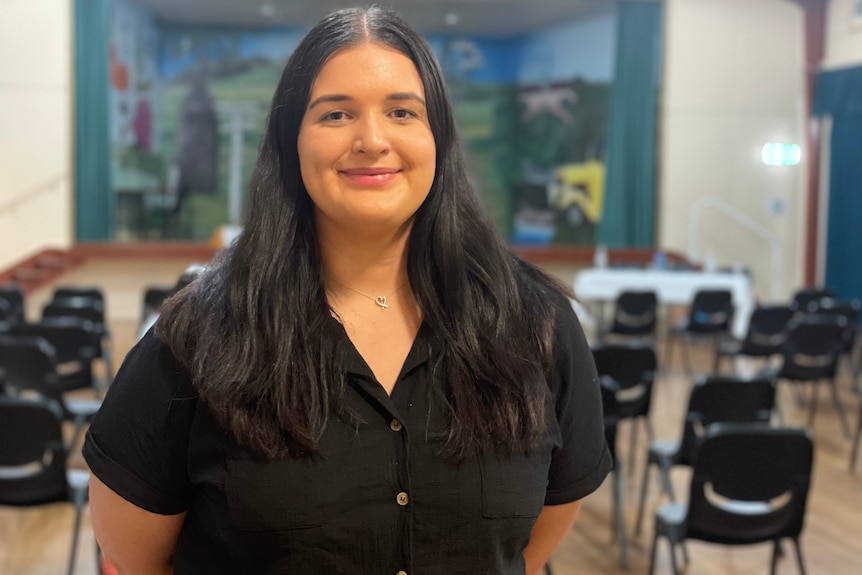 Wman with black short and long black hair smiling chairs behind her 