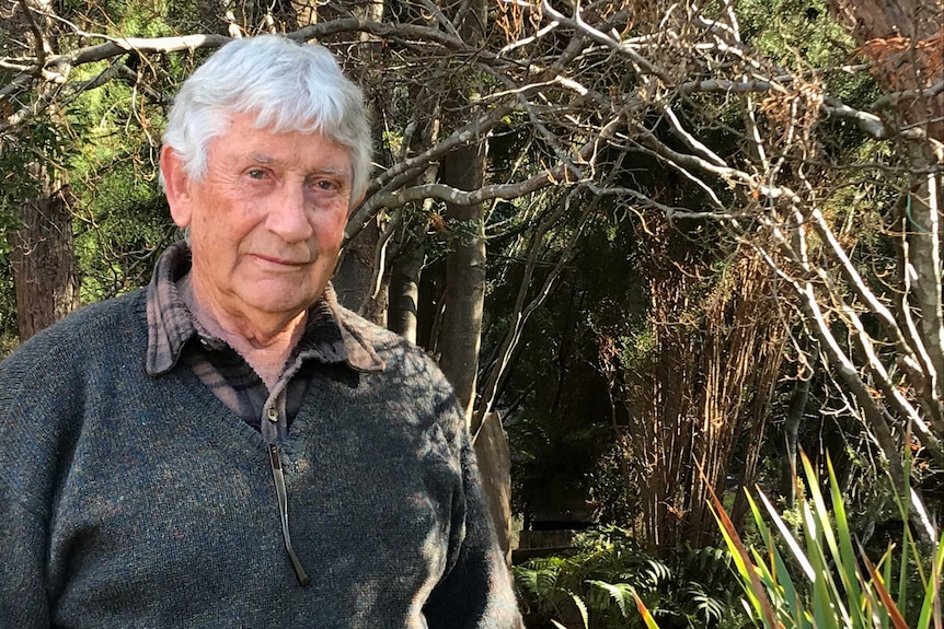 Man with white hair and a grey jumper stands in the Tasmanian bush