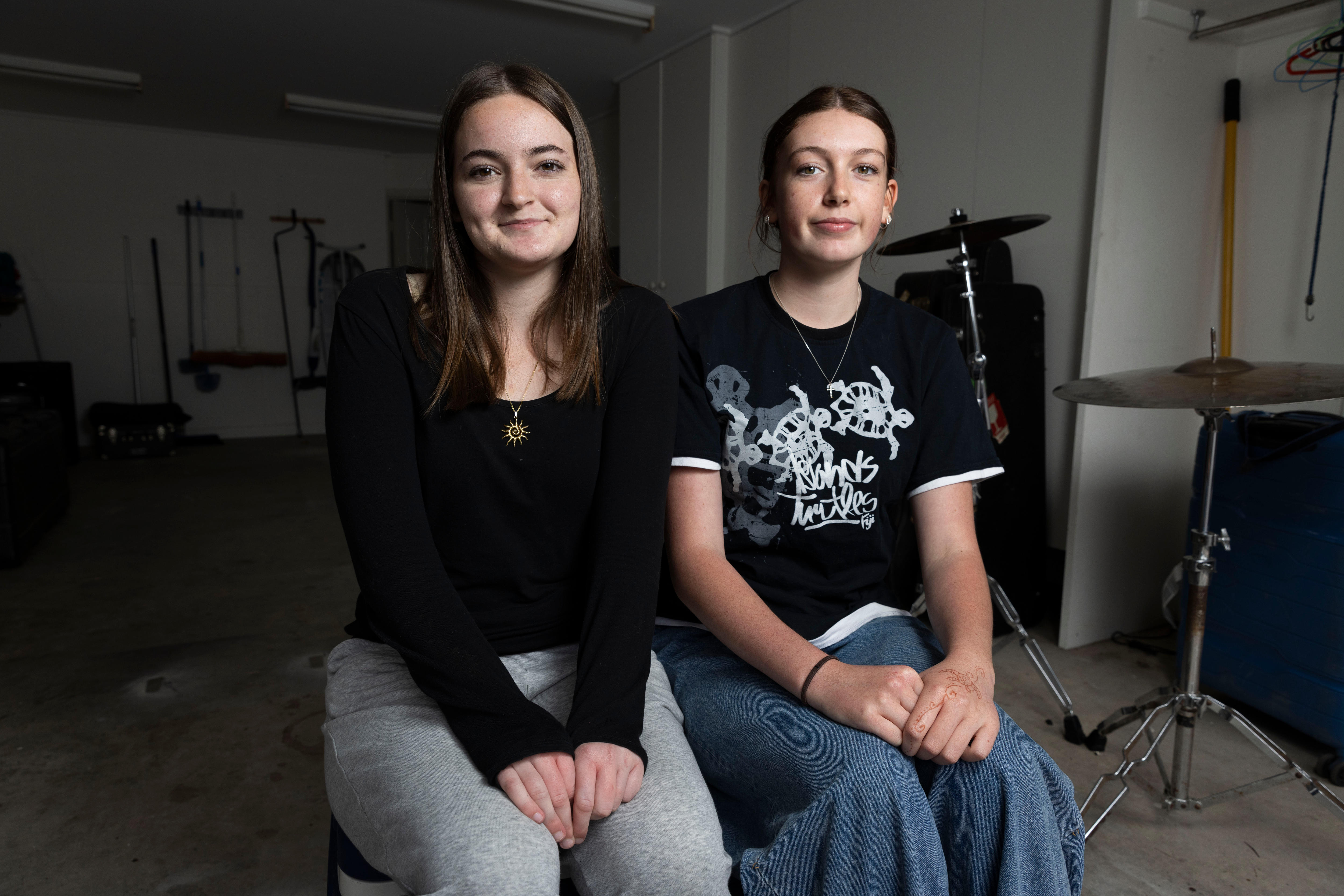 Two teenage girls sitting in a room, with musical equipment behind them.