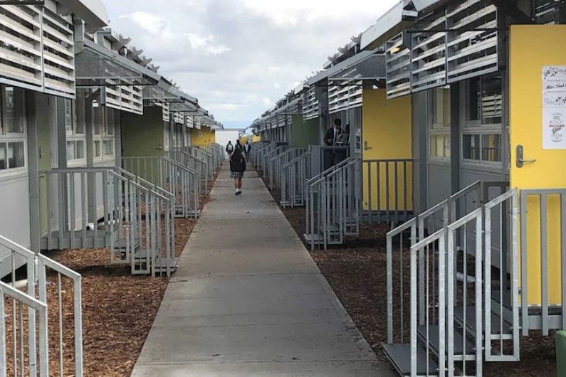 A student walks along a pathway surrounded by demountable classrooms.