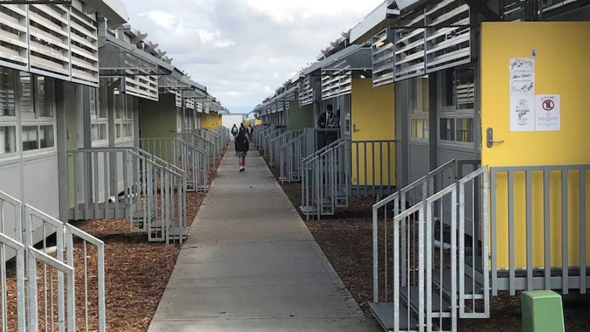 A student walks along a pathway surrounded by demountable classrooms.