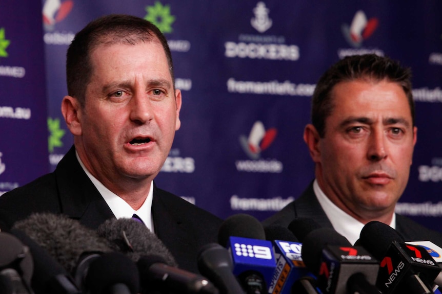 Two men at a press conference in front of sponsorship signs.