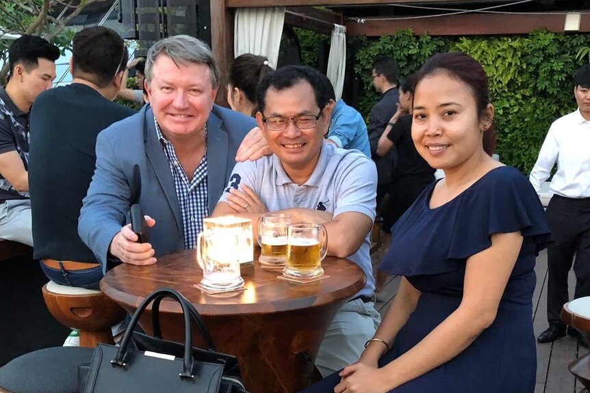Bill Clough, Kay Kimsong and Heang Tangmeng at a table, having a drink.
