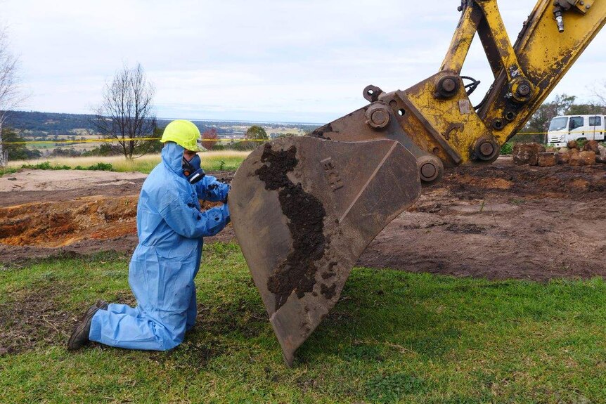 Man in hazmat suit cleaning contaminated dirt off excavator.