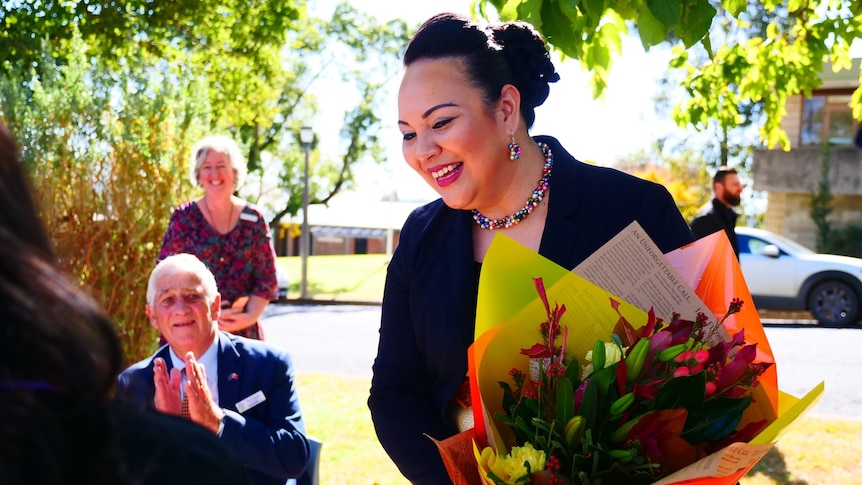  Tongan woman holds flowers, smiling.