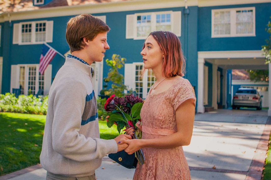Still image of Saoirse Ronan and Lucas Hedges holding hands in front of a large suburban home in Sacremento, California.