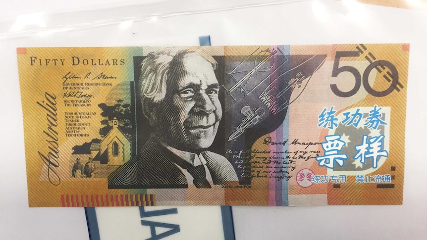 A counterfeit $50 note with blue and white Asian characters on it.