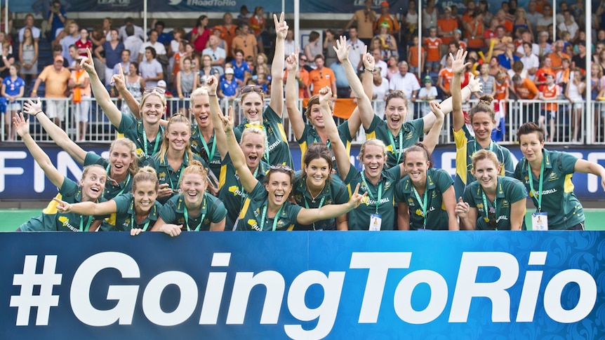 The women's hockey team pose in front of a crowd, holding a sign saying Going to Rio
