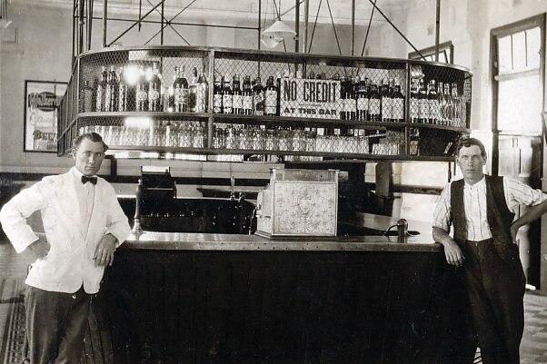 An old black and white photo of two men standing in front of an old hotel bar.