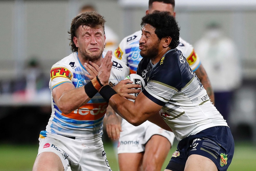 A Gold Coast Titans NRL players attempts to tackle a North Queensland opponent holding the ball.