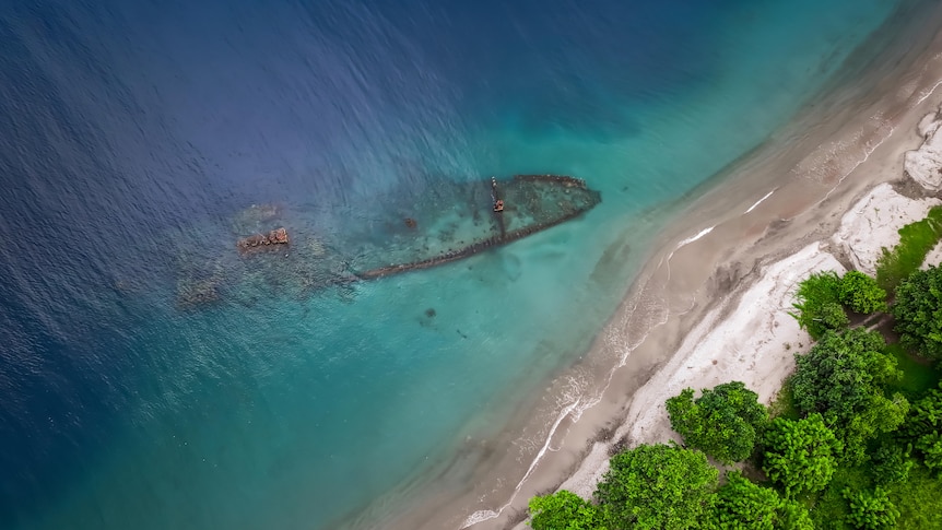 A drone shot of a mostly sunken ship wreck near a beach. 