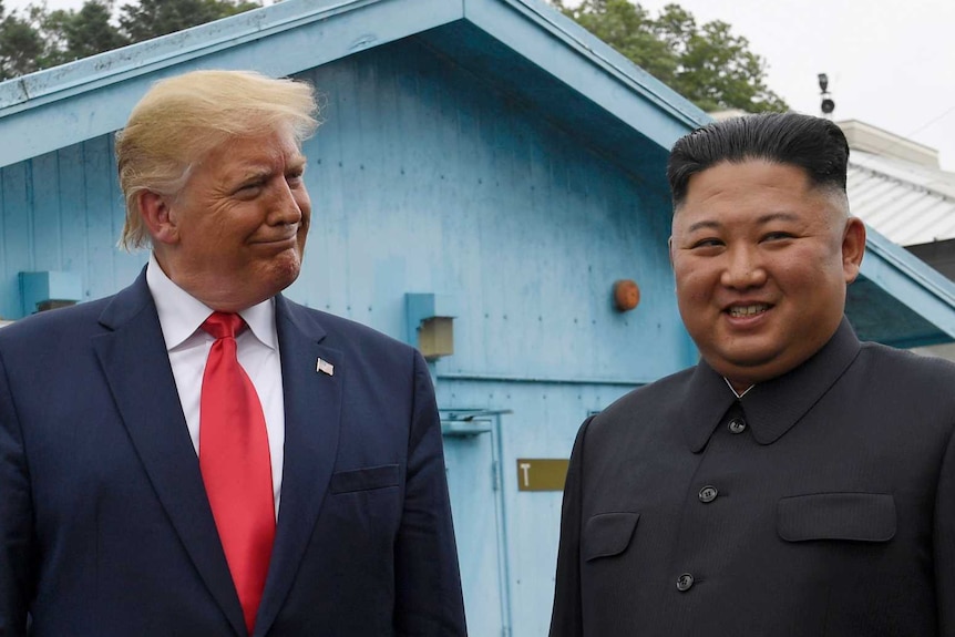 President Trump smiling at Kim Jong-un smiles and looks away