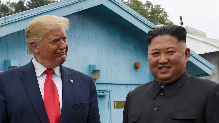 President Trump smiling at Kim Jong-un smiles and looks away